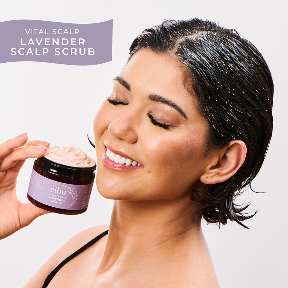 Woman with lavender scalp scrub on her hair holding a jar of the product.