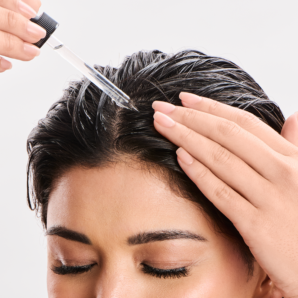 Person applying hair product with a brush on a white background